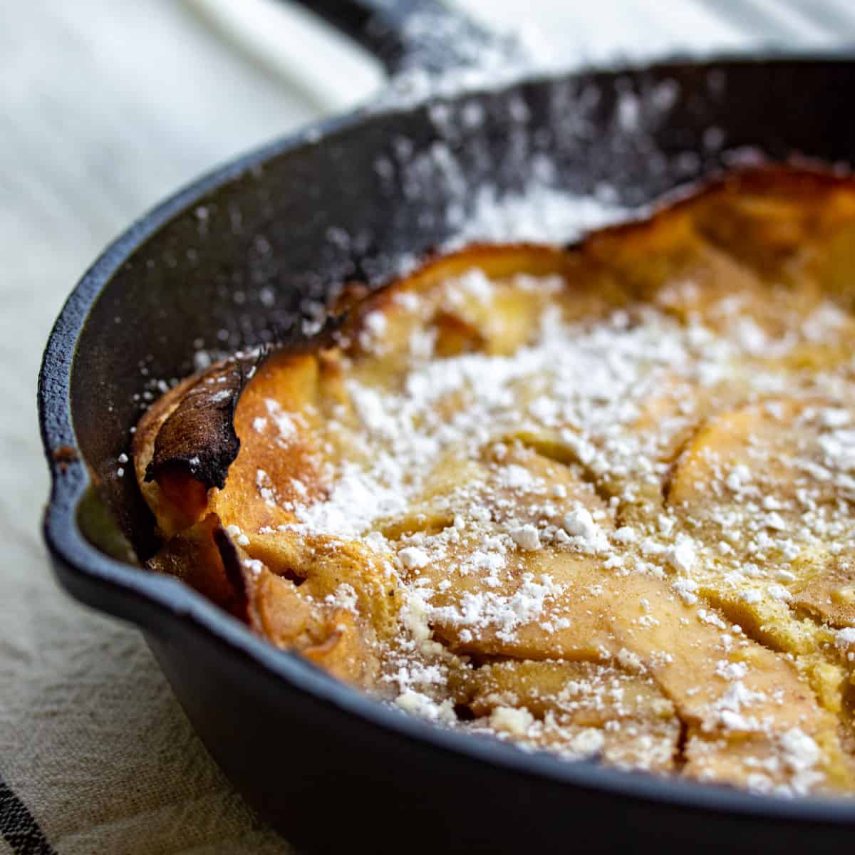 A close-up of a Dutch baby pancake in a cast iron skillet, topped with powdered sugar.