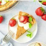 A slice of maple pie topped with whipped cream, a fresh strawberry, and mint leaves sits on a white plate next to a fork. Other pie slices, whole strawberries, and a pie dish are nearby on a light blue surface.