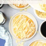 Overhead view of plates with butterhorn pastries topped with icing and almond slices, surrounded by cups of coffee, a bottle of milk, and a blue napkin. Text overlay reads “Classic Butterhorns” and website: theurbankitten.com.