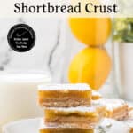 A plate with three lemon bars stacked, dusted with powdered sugar, sits next to a glass of milk. Lemons and greenery are blurred in the background. Text reads: Easy Lemon Bars with Buttery Shortbread Crust.