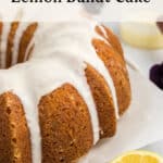 A close-up of a lemon bundt cake with white icing drizzled on top. A sliced lemon is in the foreground. Text reads Old Fashioned Dessert Lemon Bundt Cake and by theurbankitten.com at the bottom.