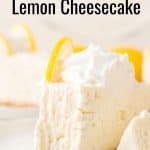A slice of creamy no-bake lemon cheesecake topped with whipped cream and a lemon slice sits invitingly on the plate, with more no-bake lemon cheesecake tempting in the background.