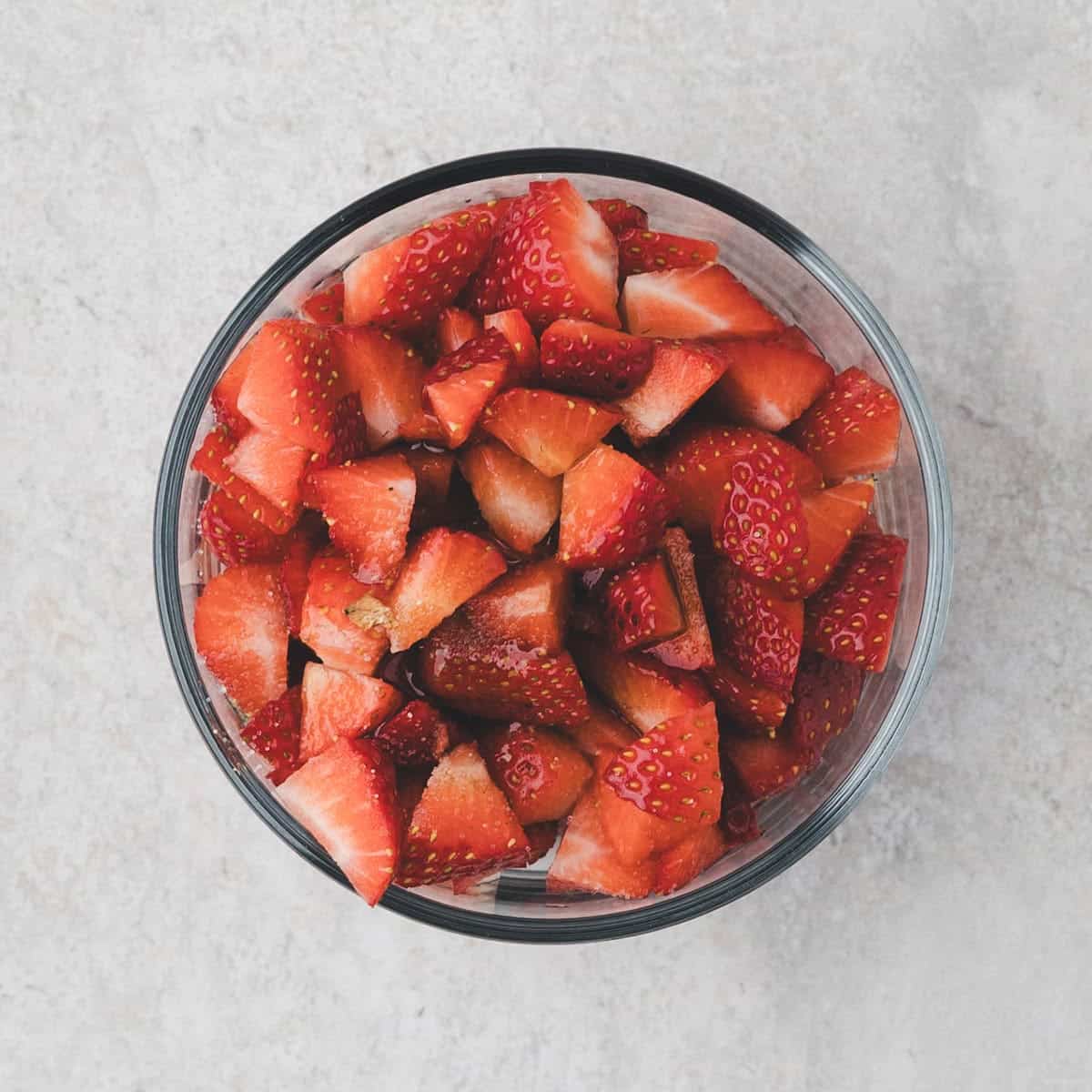 A glass bowl filled with chopped fresh strawberries, viewed from above, on a light-colored surface—perfect as a vibrant topping for a no-bake vanilla cheesecake.