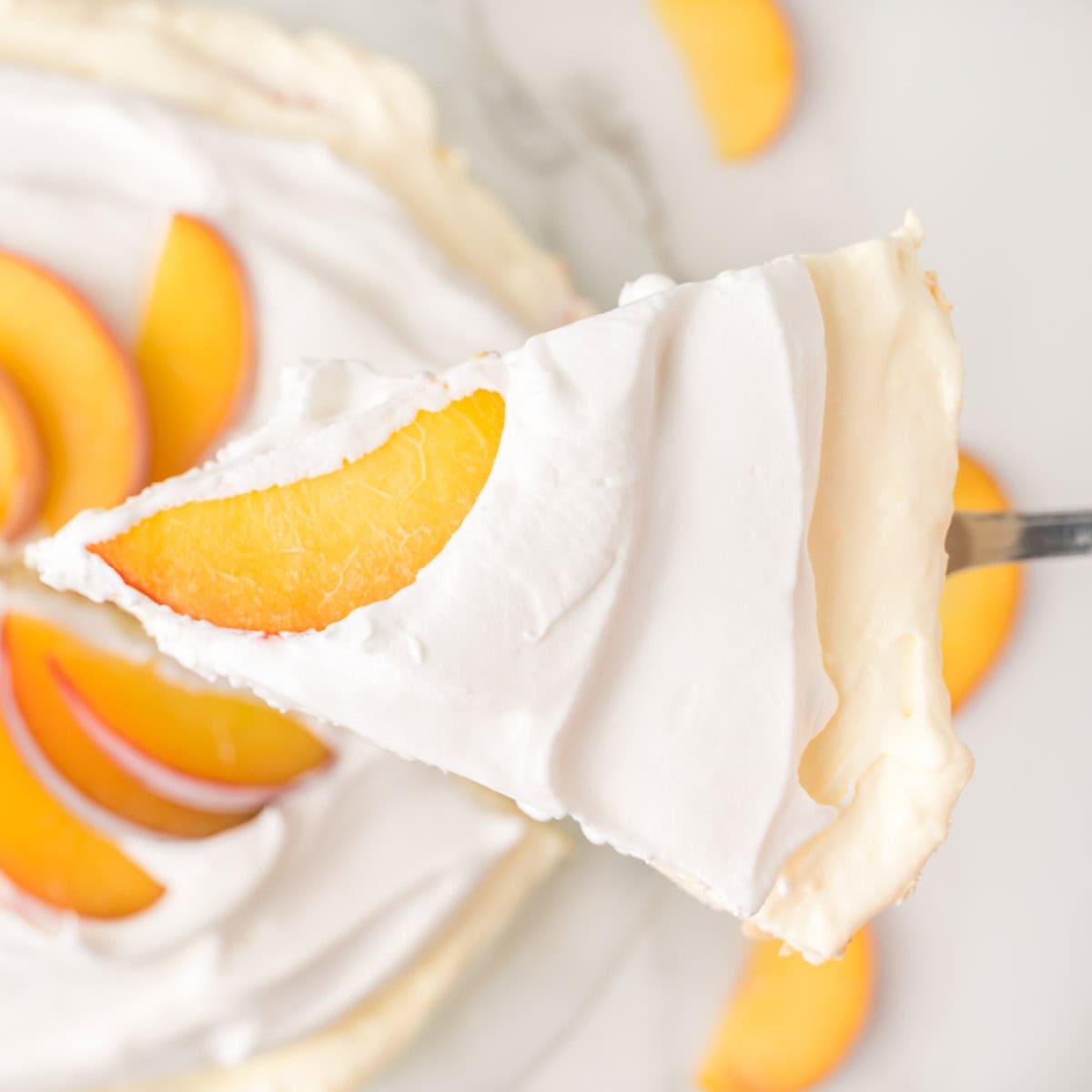A slice of creamy pie topped with whipped cream and a peach slice is being lifted from a pie garnished with more peach slices.