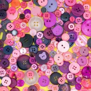 A colorful assortment of pink, purple, and black buttons in various sizes and shapes scattered on a yellow background.