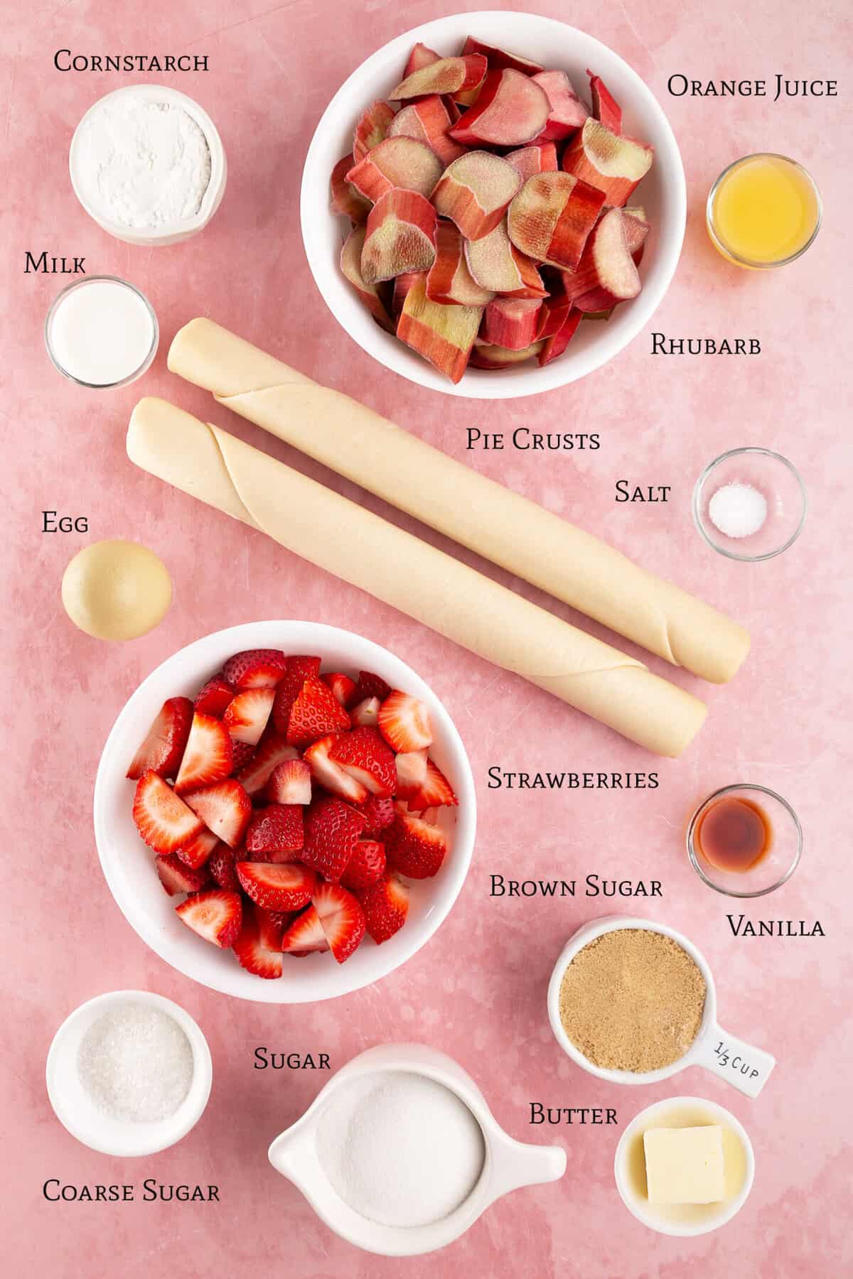 Ingredients for strawberry rhubarb pie, including rhubarb, strawberries, pie crusts, sugar, brown sugar, coarse sugar, cornstarch, milk, egg, salt, butter, orange juice, and vanilla&mdash;all beautifully arranged on a pink background to inspire your next strawberry rhubarb pie creation.
