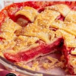 A close-up of a strawberry rhubarb pie with a golden lattice crust, a slice missing, showing the bright red filling and flaky pastry in a glass pie dish. Text reads: Strawberry Rhubarb Pie.