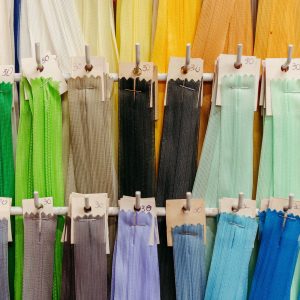 Rows of colorful zippers in various shades, including green, gray, yellow, blue, and black, are neatly displayed on hooks, each bunch labeled with a handwritten &ldquo;30&rdquo; on small cards.